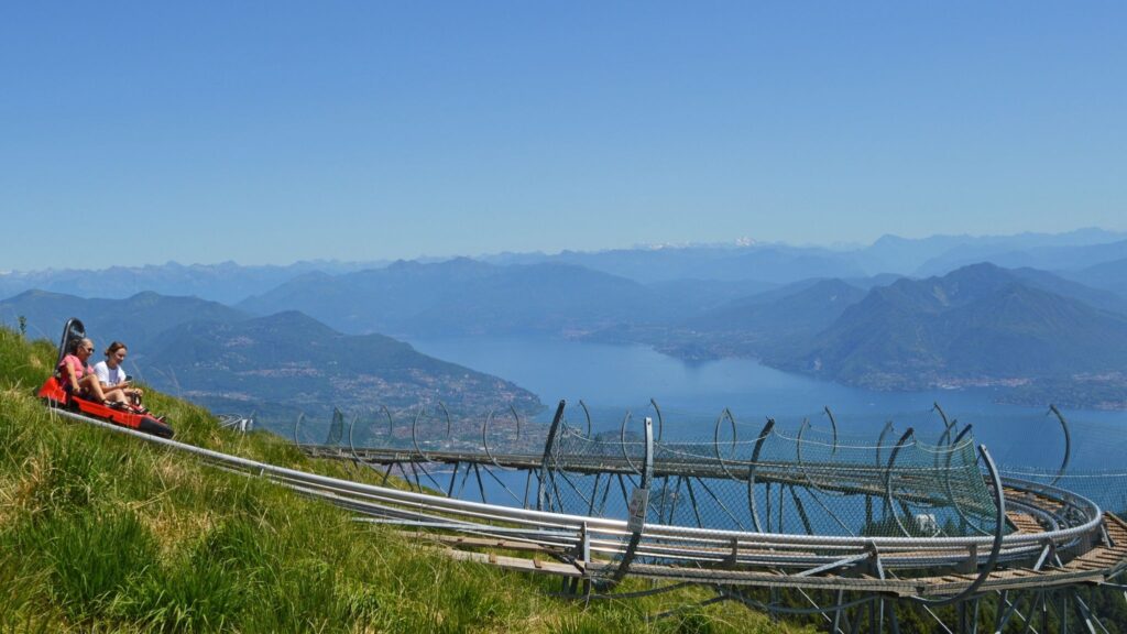 Due ragazze sul bob di Alpyland in vetta al Mottarone. Sullo sfondo si ammira in panorama su Stresa, il lago Maggio e le Isole Borromee.